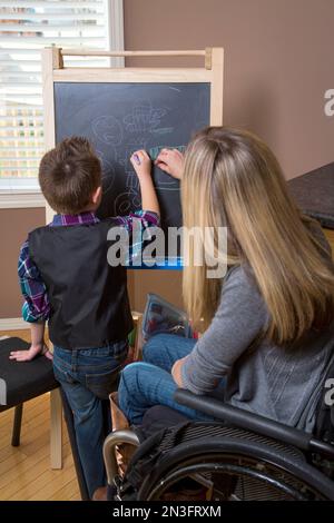 Junge Querschnittsgelähmte Mutter unterrichtete ihren Sohn und malte gemeinsam auf einer Tafel in ihrer Küche; Spruce Grove, Alberta, Kanada Stockfoto