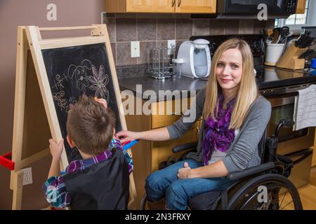 Junge Querschnittsgelähmte Mutter unterrichtete ihren Sohn und malte gemeinsam auf einer Tafel in ihrer Küche; Spruce Grove, Alberta, Kanada Stockfoto