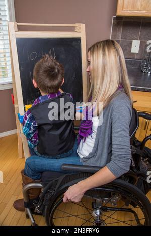 Junge Querschnittsgelähmte Mutter unterrichtete ihren Sohn und malte gemeinsam auf einer Tafel in ihrer Küche; Spruce Grove, Alberta, Kanada Stockfoto