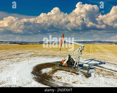 Luftaufnahme eines Kürbiss in einem schneebedeckten Feld mit dramatischen Wolken, blauem Himmel und schneebedeckten Bergketten im Hintergrund Stockfoto
