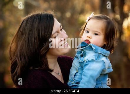 Porträt einer Mutter und ihres kleinen Mädchens mit Down-Syndrom, die während eines Familienausflugs in einem Stadtpark im Herbst eine schöne Zeit im Freien verbringen Stockfoto