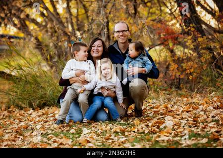 Porträt einer jungen Familie mit drei Kindern, jüngste Tochter mit Down-Syndrom, in einem Stadtpark während der Herbstsaison Stockfoto