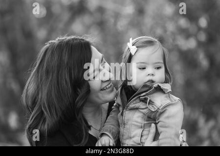 Porträt einer Mutter und ihres kleinen Mädchens mit Down-Syndrom, die während eines Familienausflugs in einem Stadtpark wertvolle Zeit im Freien verbringen Stockfoto