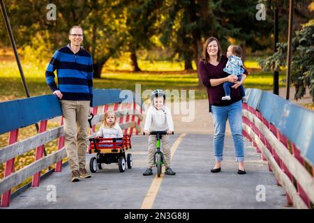 Porträt einer jungen Familie auf einer Brücke über einen Fluss in einem Stadtpark während der Herbstsaison und ihre kleine Tochter hat Down-Syndrom Stockfoto