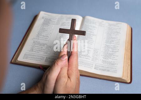 Mann, der im Hintergrund die Kreuzkreuzifx mit der offenen bibel hält. Christliches Glaubenskonzept. Stockfoto