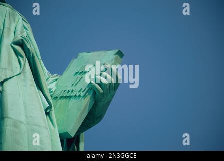 Nähere Ansicht des Buches, das von der Freiheitsstatue an einem sonnigen Tag vor einem hellblauen Himmel gehalten wird; New York City, New York, Vereinigte Staaten von Amerika Stockfoto