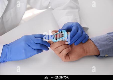 Arzt überprüft Sauerstoffgehalt des Patienten mit dem Pulsoxymeter am hellgrauen Tisch, Nahaufnahme Stockfoto
