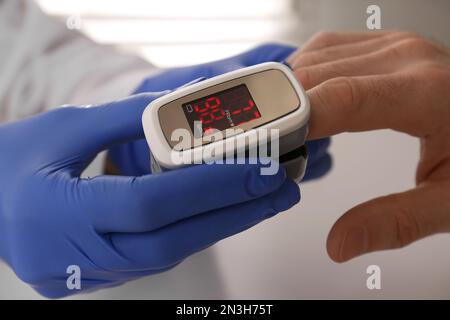 Arzt überprüft Sauerstoffgehalt des Patienten mit dem Pulsoxymeter am hellgrauen Tisch, Nahaufnahme Stockfoto