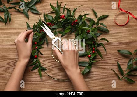 Florist macht wunderschönen Mistelkranz am Holztisch, Draufsicht. Traditionelle Weihnachtsdekor Stockfoto