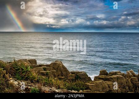 Mit den Pfannkuchensteinen im Vordergrund erscheint ein heller Regenbogen über dem Horizont über dem Meer Stockfoto