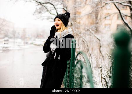 Hübsche junge Frau in warmen Kleidern, die an einem Wintertag ein Handy benutzt Stockfoto