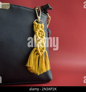 Nahaufnahme des handgefertigten Macrame-Schlüssels, der auf der schwarzen Handtasche hängt, isoliert auf rotem Hintergrund. Stockfoto