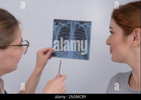 Der Arzt konsultiert eine kaukasische Frau und kommentiert die Röntgenaufnahme der Lunge. Stockfoto