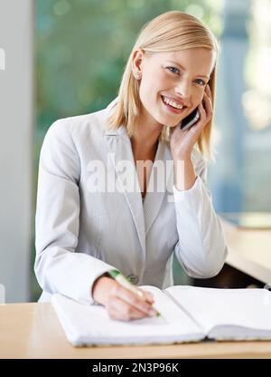 Ja, und wann möchten Sie buchen? Eine attraktive junge Geschäftsfrau, die sich Notizen macht, während sie mit ihrem Handy spricht. Stockfoto