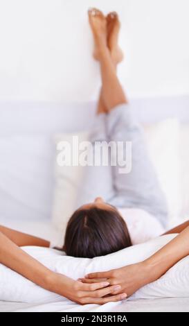 Entspannung am Morgen. Rückansicht einer jungen Frau, die auf dem Rücken ruht, mit den Beinen auf einem Kissen. Stockfoto