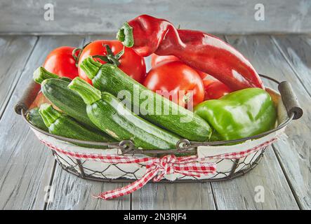 Zucchini, Paprika, Tomaten und roter italienischer Erbspfeffer im Korb auf Holzhintergrund Stockfoto