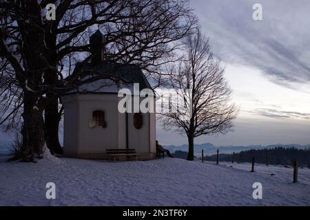 Kleine Kapelle mit Bäumen in verschneiter Winterlandschaft mit aplp-Panorama, Starnbergsee, Bayern, Deutschland Stockfoto