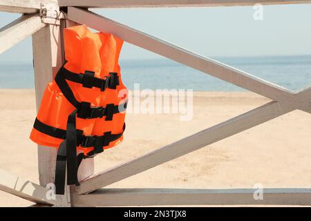 Orangefarbene Schwimmweste, die an einem Holzgeländer hängt. Rettungsausrüstung Stockfoto