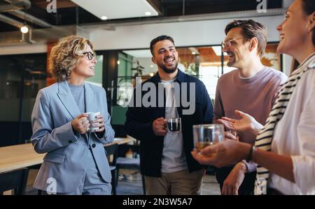 Glückliche Kollegen, die im Büro eine Kaffeepause machen. Gruppe von Geschäftsleuten, die ein Gespräch am Arbeitsplatz führen. Geschäftsleute, die in arbeiten Stockfoto