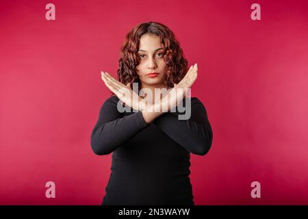 Porträt einer fröhlichen Frau in schwarzem, geripptem Kleid, isoliert auf rotem Hintergrund, gekreuzte Hände zeigen kein Stopp verbotenes Symbol, Abstoßungsexposition Stockfoto