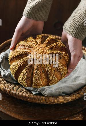 Weibliche Hände mit hausgemachtem, frisch gebackenem Brot aus Gerste und Maismehl. Vegane und vegetarische gesunde Ernährung Konzept. Dunkler rustikaler Stil. Stockfoto