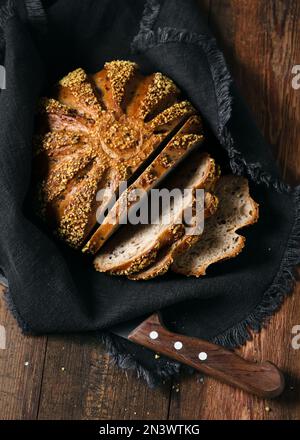 Draufsicht auf geschnittene Vollkorngerste und Maisbrot auf einer dunklen Leinenserviette mit Messer auf rustikalem Holzhintergrund. Speicherplatz kopieren. Stockfoto