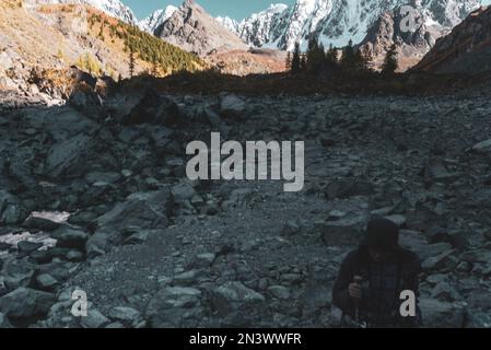 Ein Mädchen mit Wanderstöcken wandert am Abend bei Sonnenuntergang entlang der Steine eines ausgetrockneten Bergsees im Schatten der Berge in Altai Stockfoto