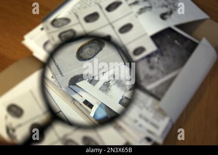 Fingerabdruckkarte auf dem Tisch, Blick durch Lupe. Detektivarbeit Stockfoto