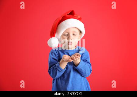 Süßer kleiner Junge mit Weihnachtsmannmütze auf rotem Hintergrund Stockfoto