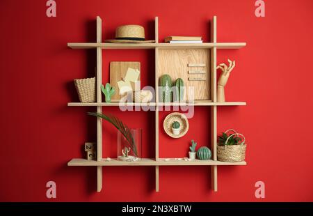 Elegante Holzregale mit dekorativen Elementen an roten Wänden Stockfoto