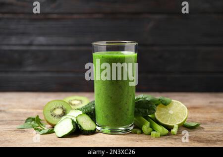 Köstlicher grüner Saft und frische Zutaten auf einem Holztisch vor schwarzem Hintergrund Stockfoto