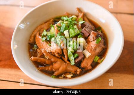 Hähnchensuppe mit Hähnchenschenkelfüßen und Flügeln in roter Suppenschüssel und Gemüsebohnzwiebeln - mit chinesischen Kräutern eingeschmort Stockfoto