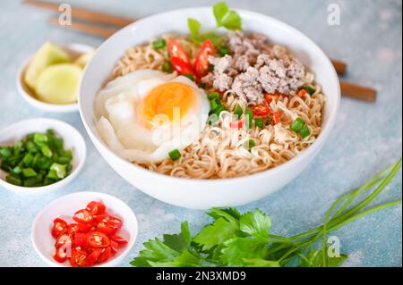 instant-Nudeln kochen leckeres Essen mit Schüssel, Nudelschüssel mit gekochtem Ei Hackfleisch Schweinefleisch Gemüse Frühlingszwiebeln Zitronen Limetten Salat Sellerie und Chili on Stockfoto