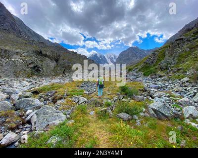 Ein Mädchen mit Rucksack wandert auf einem steinernen Pfad im Altai-Gebirge vor dem Hintergrund von Gletschern und Schnee im Sommer. Stockfoto