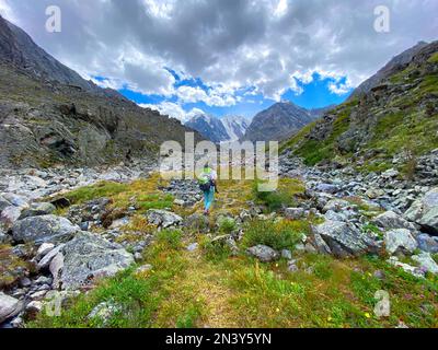 Ein Mädchen mit Rucksack wandert auf einem Bergweg im Altai-Gebirge vor dem Hintergrund von Gletschern und Schnee im Sommer. Stockfoto