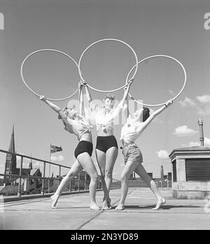 Gymnastik in den 1940er Jahren. Drei junge Turnerinnen stehen auf einem Dach in Stockholm und bilden ein symmetrisches Bild, wenn sie die drei Ringe über sich halten und posieren. Schweden 1945 Kristoffersson Ref O143-4 Stockfoto