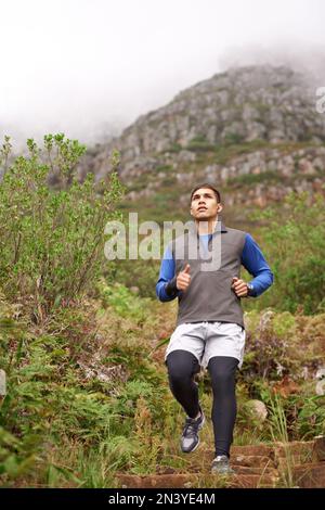Von hier geht es bergab. Ein junger Mann, der bergab auf einem Bergweg rennt. Stockfoto