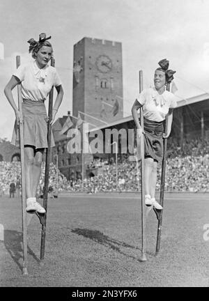 1950er Paar. Schauspielerin Sickan Carlsson rechts und ein Freund laufen und balancieren auf Stelzen auf dem Rasen des Stockholmer Stadions. Schweden 1939 Stockfoto