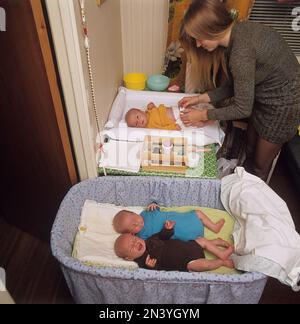 1970er Mutter. Eine Frau putzt und wechselt Windeln auf ihren drei Babys, die auf einem Wickeltisch liegen. Sie hat Drillinge und zwei sind im Bett. Schweden 1972 Ref. BV105-2 Stockfoto