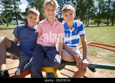 Wir wollten, bis es schwindelig war. Ich wollte mitmachen. Eine Gruppe kleiner Jungs, die auf einem Spielplatz sitzen. Stockfoto