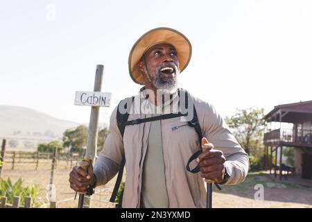 Überraschter afroamerikanischer Seniorenmann mit Wanderstöcken, die an Land vor klarem Himmel spazieren Stockfoto