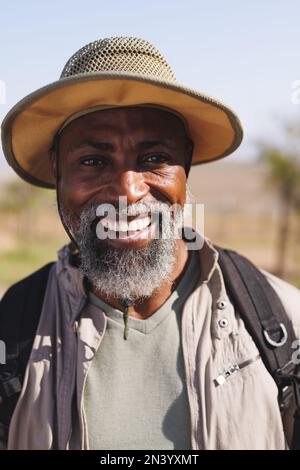 Porträt eines lächelnden afroamerikanischen Seniors mit Hut beim Wandern unter klarem Himmel aus nächster Nähe Stockfoto