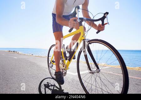 Genießen Sie die Landschaft beim Training. Beschnittene Ansicht eines Radfahrers, der entlang einer Meeresstraße radelt. Stockfoto