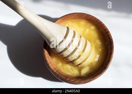 Honigstiel in einer Holzschüssel mit Honig in der Sonne. Gesunder Bio-dicker Honig Dippen aus einem Holzlöffel Honig, Nahaufnahme. Harter Schatten. Stockfoto
