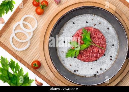 Rohes Rinderfleisch Burger Steak Cutlets in einer Gusseisenpfanne auf einem Holzbrettgrund. Schnittlauch für Burger mit Gemüse und Gewürzen. Fastfood Stockfoto