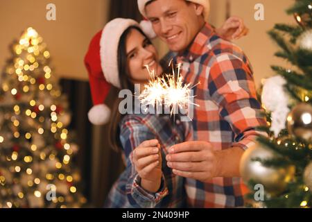 Ein Paar mit Glitzer im Weihnachtszimmer, das sich auf Feuerwerk konzentriert Stockfoto
