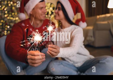 Ein Paar mit Glitzer im Weihnachtszimmer, das sich auf Feuerwerk konzentriert Stockfoto
