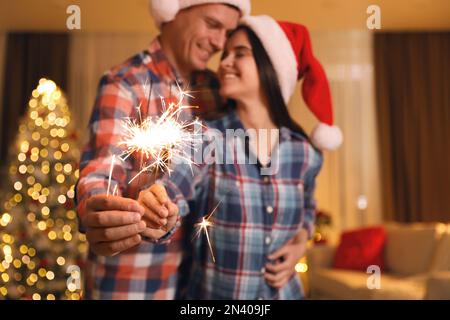 Ein Paar mit Glitzer im Weihnachtszimmer, das sich auf Feuerwerk konzentriert Stockfoto