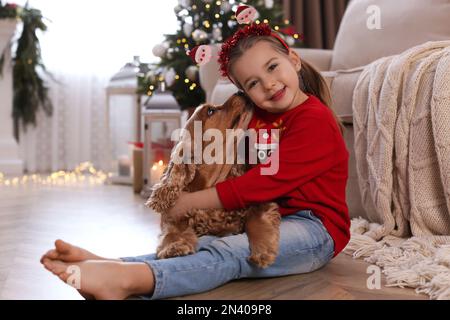 Süßes kleines Mädchen mit englischem Cocker Spaniel im Zimmer, dekoriert für Weihnachten Stockfoto