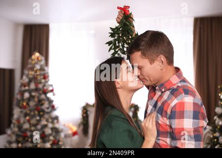 Ein Paar küsste sich unter Mistelzweigen in einem zu Weihnachten dekorierten Zimmer Stockfoto